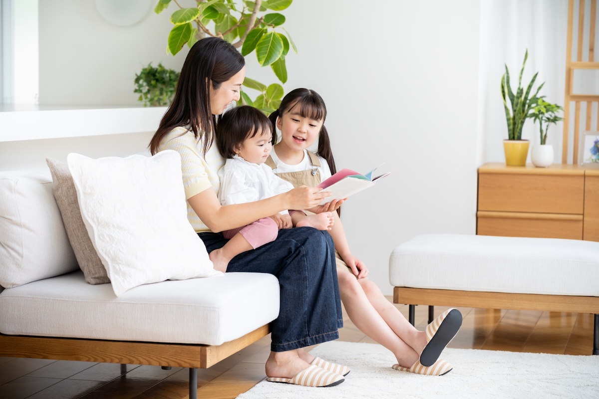 母親が2人の子どもと一緒にソファに座り、絵本を読み聞かせている。